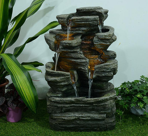 Multi-level rock cascading rock fountain is placed between potted plants.